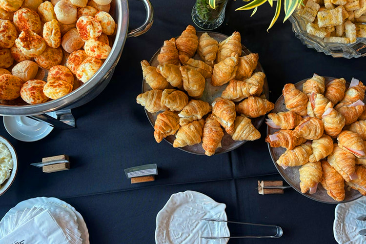 Mesa de coffee break corporativo com mini croissants, salgados e acompanhamentos organizados para eventos empresariais